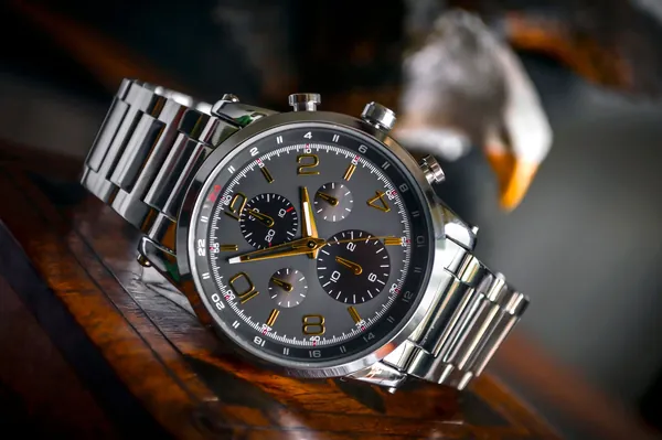 Montre chronographe en acier à cadran gris et aiguilles dorées sur une surface en bois sombre