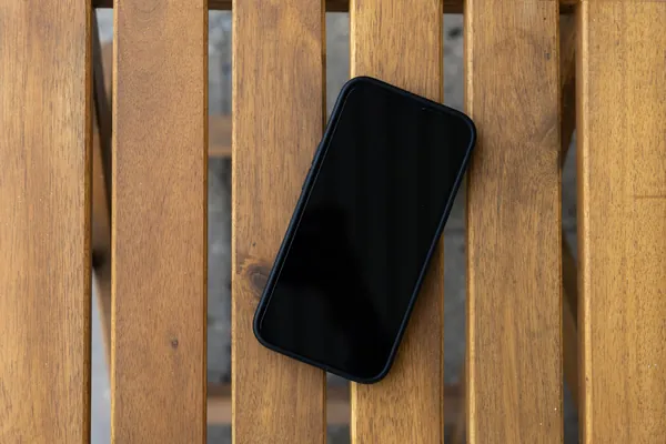 Smartphone noir à écran éteint posé à plat sur des lattes de bois