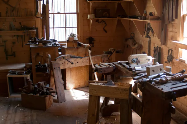 Atelier de menuiserie : établis en bois, outils accrochés au mur et lumière venant des fenêtres