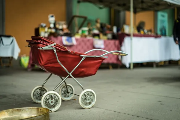 Ancien landau de poupée rouge à roues blanches devant les stands d'un marché aux puces