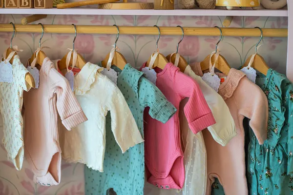 Petits vêtements de bébé aux couleurs pastel suspendus sur des cintres en bois