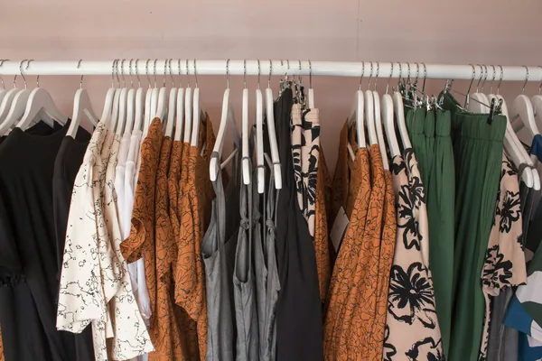 Portant de vêtements pour femme : chemisiers à motifs, hauts unis, robe imprimée et pantalon vert sur cintres blancs