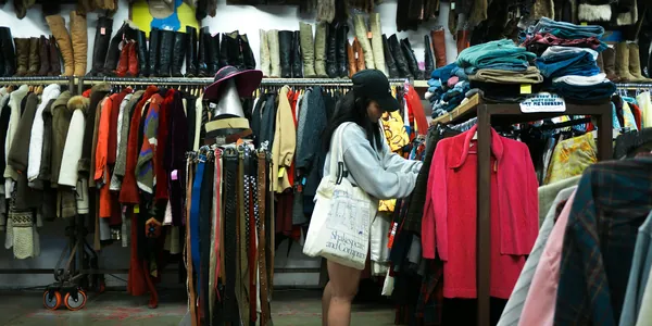 Intérieur d'une friperie : portants chargés de vêtements de toutes les couleurs et piles de pulls en hauteur
