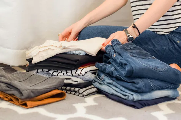 Vêtements pliés en piles sur un lit pendant un tri : jeans, t-shirts rayés et pulls