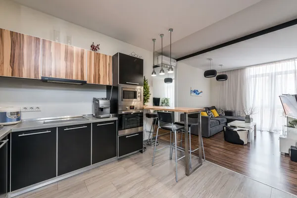Appartement à pièce de vie ouverte : cuisine aux façades noires et bois, îlot et tabourets hauts