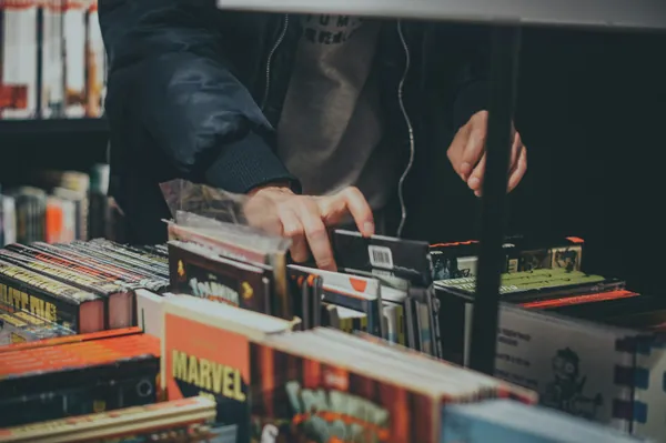 Mains qui parcourent des bacs de disques vinyles et de bandes dessinées chez un disquaire