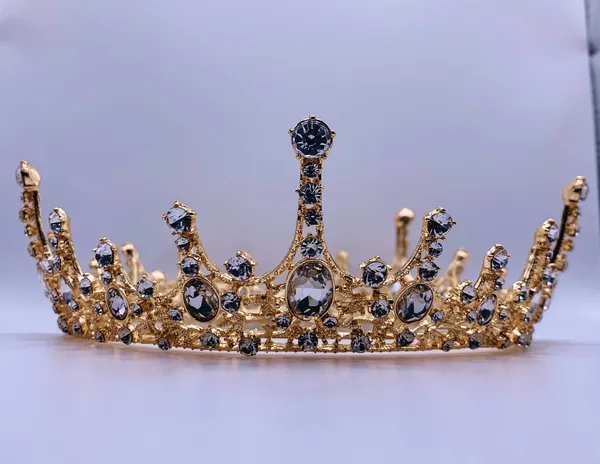 Diadème doré serti de pierres sombres et de strass sur un fond mauve clair