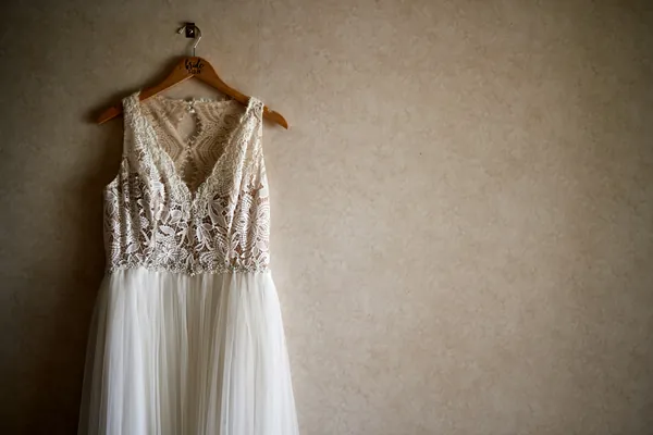 Robe de mariée blanche à bustier en dentelle et jupe en tulle suspendue contre un mur beige