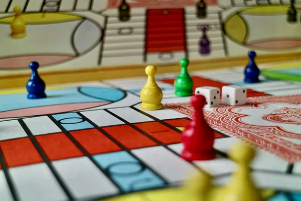 Plateau de jeu de société coloré avec des pions bleu, vert, jaune et rouge et deux dés blancs