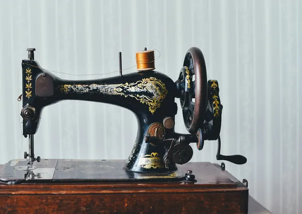 Machine à coudre ancienne noire à décor doré et volant manuel, posée sur un meuble en bois